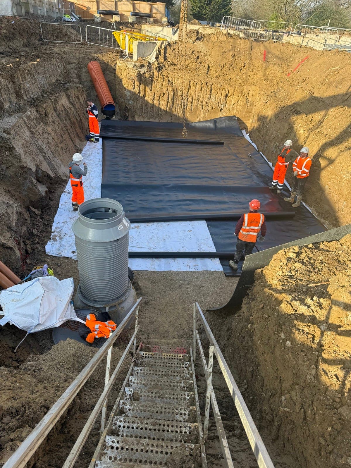 Aquatech crew installing the 150m³ attenuation tank membrane in a deep excavation at Enfield
