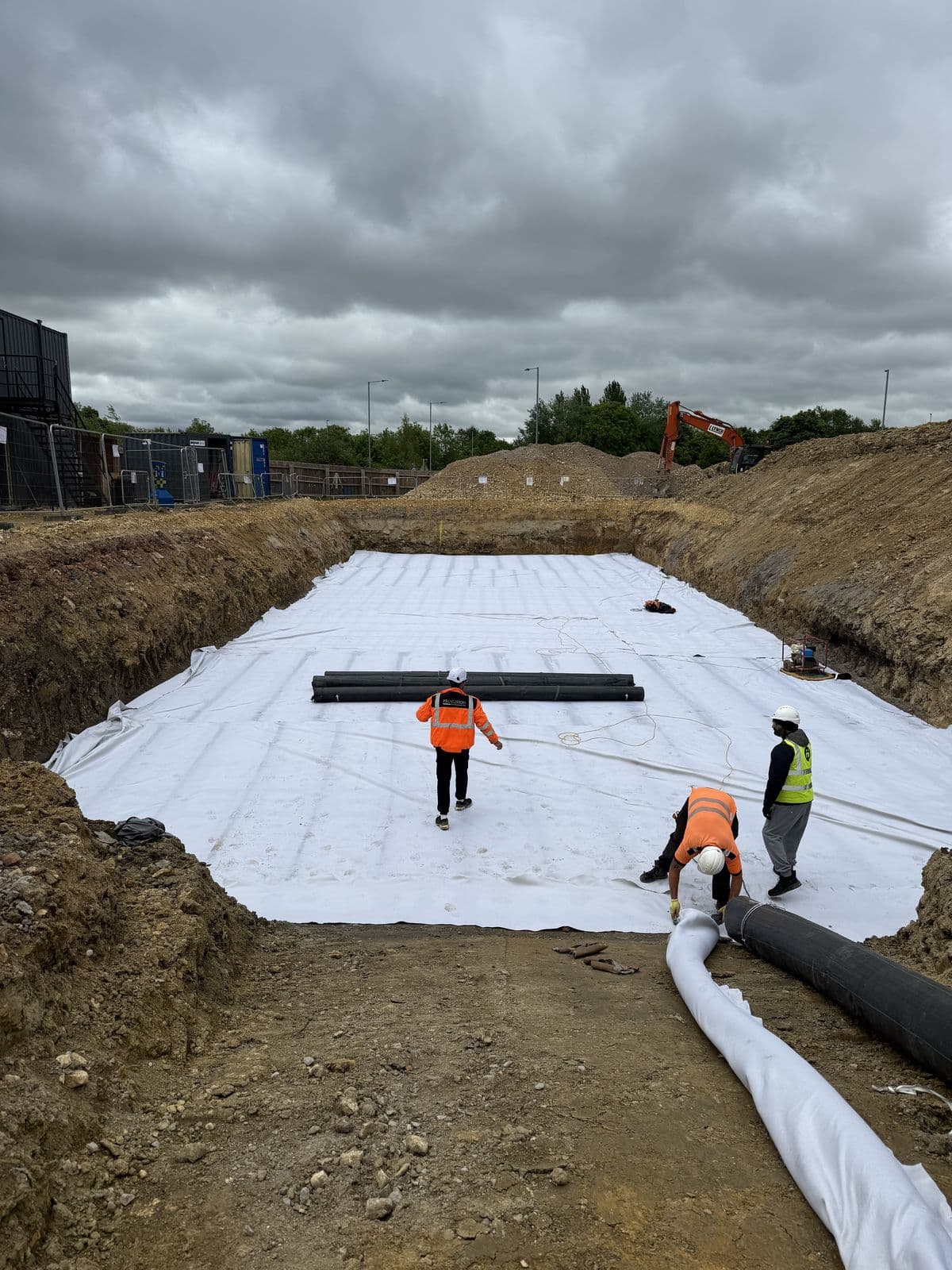 Aquatech crew rolling out geotextile across the base of the 673m³ tank excavation at Lidl Corby